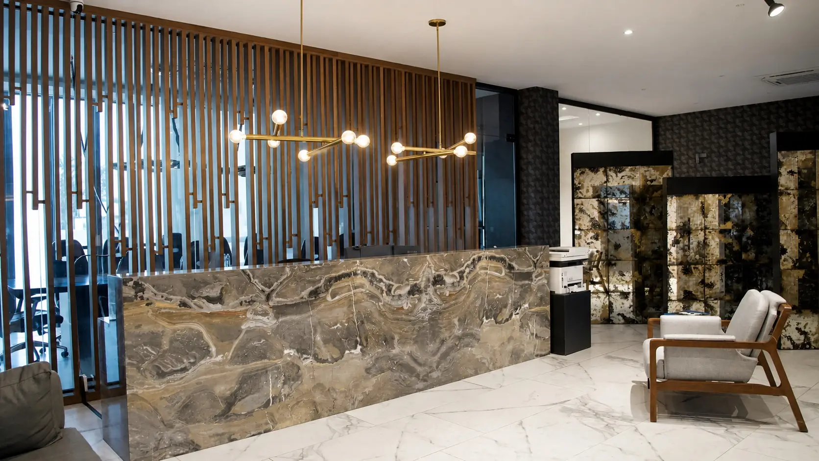 Recepción de Concordia Patrimonial: mostrador de mármol veteado, celosía de madera, lámpara de latón y sillón de espera.
