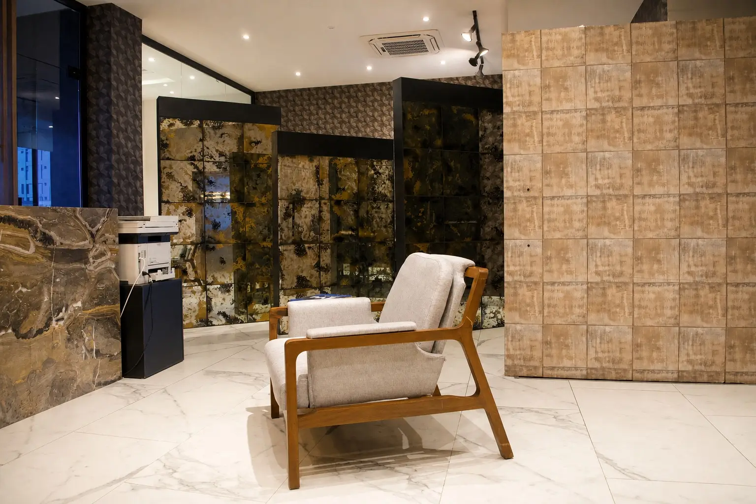 Área de espera de Concordia Patrimonial: sillón de madera y tapiz claro sobre piso de mármol, frente a paneles decorativos en tonos ámbar.