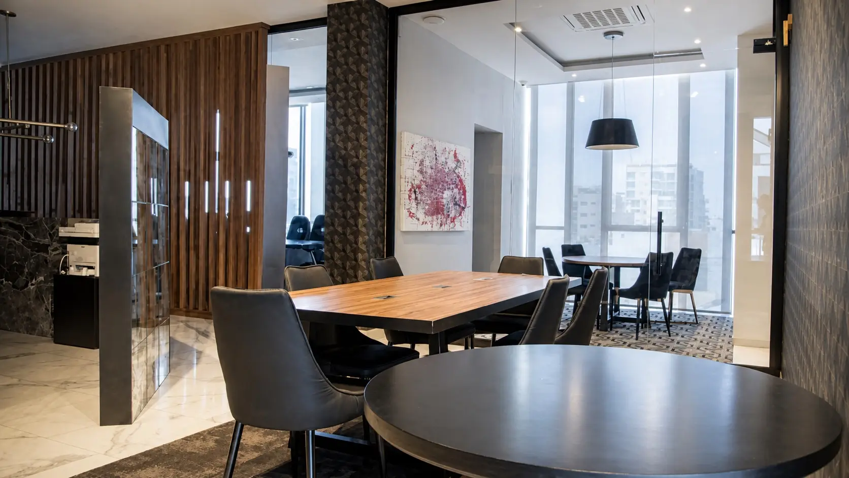 Sala de reuniones de Concordia Patrimonial: mesa de madera para seis personas, mesa redonda junto al ventanal y celosías de madera que separan el área de trabajo.
